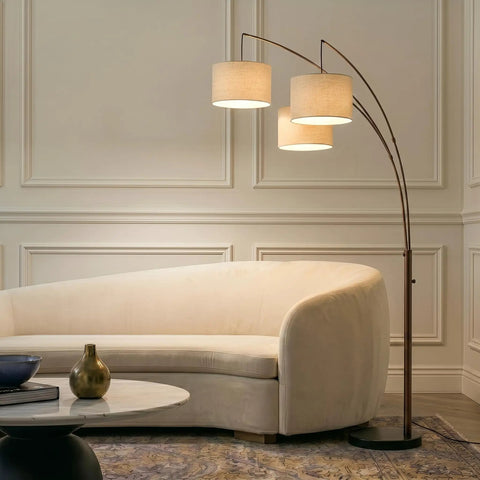 Trilage Arc Floor Lamp With Three Fabric Shades And LED Bulbs illuminated over a sofa in a living room, oil rubbed bronze finish