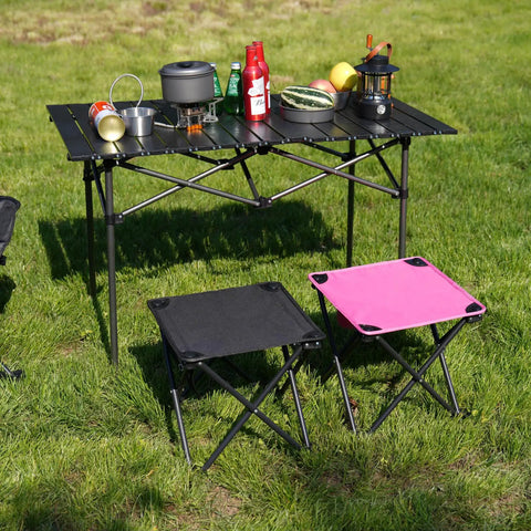 2 Pack 13 Inch Portable Folding Camping Stool With Carry Bag For Outdoor Adventures Camping Hiking Beach Fishing Gardening Picnics And Travel Ultralight Lightweight Grab And Go Foot Stool, black and pink stools next to camping table.