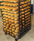 Bakery oven rack with high-temp swivel caster wheels full of freshly baked baguettes on mesh trays.