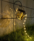 Sun Powered Watering Can Lights For Garden With Cascading LED Pouring Water Effect lighting a garden wall at night