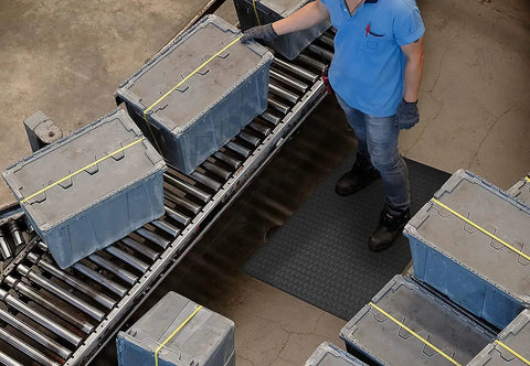 Built Different And Tough As Nails Anti Fatigue Mat With Heavy Duty Diamond Texture For Standing All Day Without Breaking A Sweat Grease And Oil Resistant Commercial Closed Cell Foam Ergonomic Work Pad In Black Three By Five Feet under worker with boxes on conveyor.
