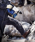 Side view of blue and white SDS Plus hammer drill with long masonry bit at rocky construction site.