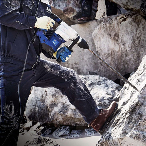 Side view of blue and white SDS Plus hammer drill with long masonry bit at rocky construction site.