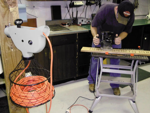Wonder Winder Grab And Go Hand Crank Extension Cord Winder in a workshop setting, orange cord visible, person working nearby