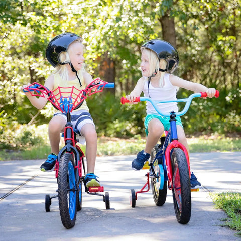 Two children riding bikes with training wheels in a park, wearing helmets and casual clothing.