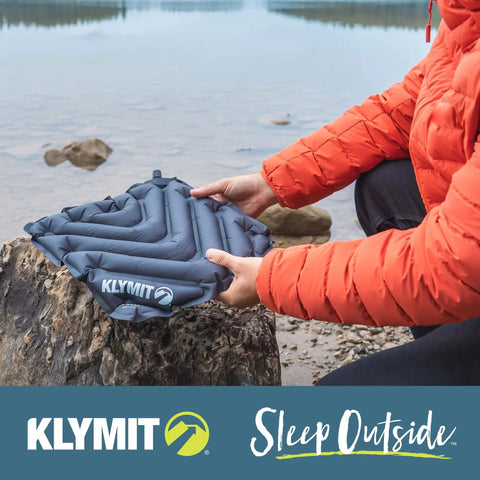 Person holding V Seat Inflatable Cushion For Travel, Camping, Backpacking And Bleachers by a lakeside with rocks.