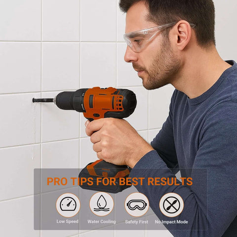 Cordless drill with glass-tile drill bit in use by man wearing safety glasses, side view against white tiles.