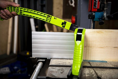 Front view of neon‑green BOW PushPRO PP1 EVA‑tipped push block guiding a grooved metal board on a table saw