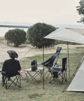 Person sitting on ultra lightweight folding camping chair with carry bag by the beach, surrounded by other camping gear.