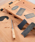 Top Shelf Six Piece Cabinet Scraper And Burnisher Kit With Blue Spring Steel Blades Plus Hardened High Speed Steel Sharpening Rod laid out on a workbench.