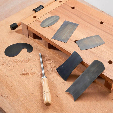 Top Shelf Six Piece Cabinet Scraper And Burnisher Kit With Blue Spring Steel Blades Plus Hardened High Speed Steel Sharpening Rod laid out on a workbench.