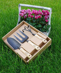 Three Piece Garden Tool Gift Set With 3 Tine Cultivator Forged Trowel And Forged Hand Fork on grass next to pink flowers