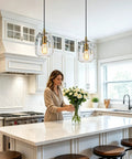 Pendant Lights Kitchen Island, Hand-Blown Clear Glass Brass Gold 9 Inch H illuminating a kitchen with a woman arranging flowers.
