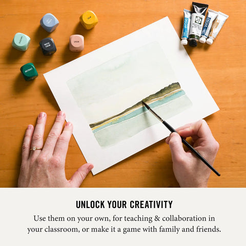 Art Dice Prompts Set Of Nine Wood Dice For Drawing And Painting Inspiration, Color Coded, One Inch Each, Roll To Kickstart Creativity And Bust Artist Block With Easy Read Prompts. Wood art prompt dice beside watercolor painting and paint tubes
