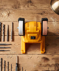 Slick Cordless Mini Bench Grinder With 70mm Wheel And 5500 RPM For Quick Sharpening And Polishing Jobs Around The Shop No Wire Hassle Just Drop Your 18V Pack And Roll on a wooden table with tools.