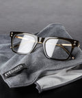 Glasses cleaning cloth (30 × 20 cm) microfiber gray with EYESHAKER logo, shown with eyeglasses.