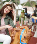 Person sitting on a carousel horse, smiling outdoors in a casual outfit with surrounding colorful horses.