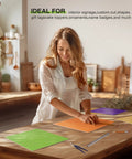 Woman creating with 7 Pack Rainbow Colored Plywood Sheets 12 By 12 By One Eighth Inch 3mm Thick Unfinished Wood For Laser Cutting And Engraving DIY Craft Kits For Ornaments Models Drawing And Wood Burning Projects in a workshop.