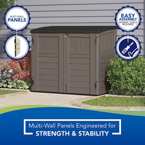 34 Cu Ft Horizontal Resin Storage Shed With Floor Included For Outdoor Use Weatherproof And Lockable Fits Small To Medium Trash Cans Generators And Garden Tools Stoney Black next to a shrub with wall backdrop.