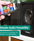 Powered Bookshelf Speakers With Built-In Amplifier And 3-Inch Drivers For Turntables, TV, PC, And Wireless Music Streaming Bluetooth 5, RCA, And Aux Dope, Warm, Versatile Home Audio System next to a smartphone for wireless connection.
