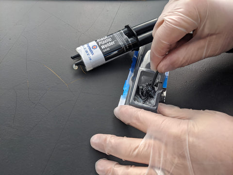 Black Plastic Weld Adhesive For Plastics Ceramics And Wood, Fast-Curing Structural Bond Up To 3500 Psi, Sets In Five Minutes, syringe with gloved hands