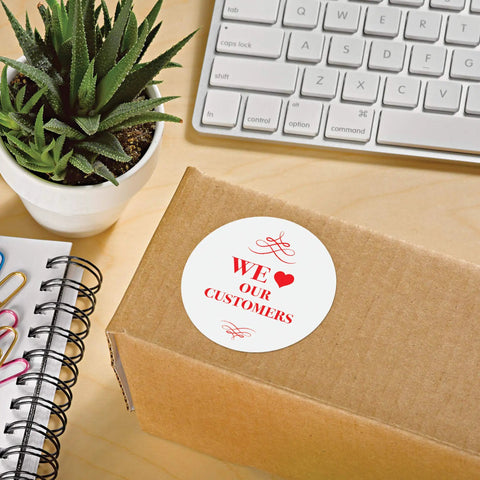 Round Printable Labels 300 Pack 2.5 Inch Matte White Stickers on a cardboard box with plant and stationery.