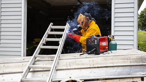 Person welding with K4134-1 Welding Helmet With Brown Plastic Shell, Ratchet Headgear, Auto Darkening Lens, alongside metal ladder