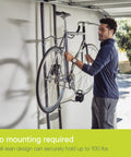 Man using Rugged Two Bike Gravity Rack For Garage And Home No Drilling Required Fully Adjustable Leaning Wall Space Saver Bike Storage Stand Holds Up To 100 Lbs For Any Style Bicycle Or Ebike in a garage.