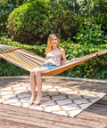 Cotton Double Hammock With 55 Inch Spreader Bar Portable Camping Hammock With Carrying Bag And Tree Straps For Patio Backyard Or Balcony 450 Pound Capacity Brown And Khaki For Easy Hangout Chill Sessions, set up in garden with a person sitting.