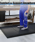 Person standing on a 3 By 7 Foot Anti Fatigue Floor Mat Extra Thick One Inch For Machinist Shop Garage Standing Pad with black anti-static rubber top in workshop.