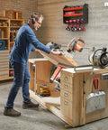 Man using saw in workshop with Heavy Duty Wall Mount Drill Organizer and Cordless Tool Storage Rack visible on wall