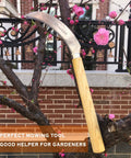 Grass Sickle With Sawtooth Design And Japanese Weeding Hoe For Garden Work High Tough Stainless Steel With Solid Wood Handle Ergonomic Grip Yellow Handle Perfect For Weeding Loosening Soil Pruning And A Great Gift For Garden Lovers displayed against a tree with pink blossoms.