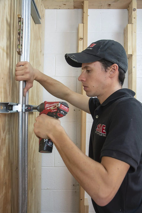 Person using a power drill on a wooden frame, focusing on the installation of a steel connector plate