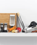 Kitchen tools with Stainless Steel Salt And Pepper Grinder Set for kitchen and table, cutting board, slicer, and vegetables on a shelf.