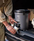 Person pouring from Hardcore Two Gallon Insulated Water Jug Featuring Double Wall Foam Build into a cup, perfect for outdoor activities.