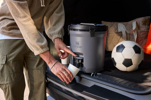 Person pouring from Hardcore Two Gallon Insulated Water Jug Featuring Double Wall Foam Build into a cup, perfect for outdoor activities.