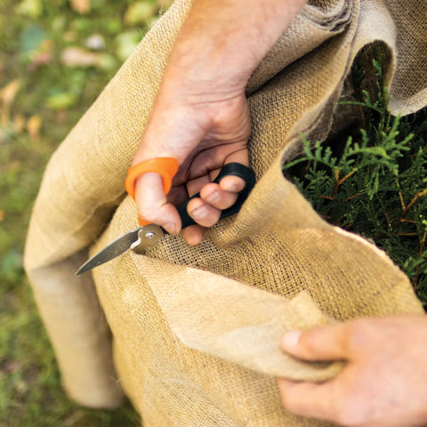 All In One Garden Tool 7-In-1 Pruning Shears in use cutting burlap around plant, showcasing titanium knife and ergonomic handle.
