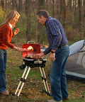 Two people cooking on a Portable Gas Grill With VersaStand For Camping And Backyard BBQ 150 Sq In Cooking Surface 5500 BTU Burner