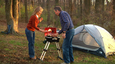Two people cooking on a Portable Gas Grill With VersaStand For Camping And Backyard BBQ 150 Sq In Cooking Surface 5500 BTU Burner