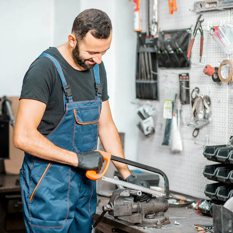 Stainless steel tube being cut on a workbench vise by a worker in blue overalls.