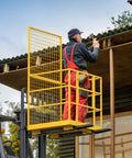 Forklift safety cage; side view of yellow metal cage with mesh panels mounted on forklift for elevated work.