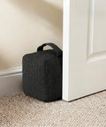 Heavy Duty Weighted Door Stopper With 4.4 Lb Internal Weight keeps door stable, resting against a white door on carpeted floor.