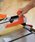 Hand using an orange three quarter inch V notch push stick for narrow stock on table saw, part of Must Have Power Tool Safety Set For Woodworking With Foam Grip Push Blocks Extra Long 16 Inch Push Block With Dual Handles Three Quarter Inch V Notch Push Stick For Narrow Stock And Eight And A Half Inch Saw Guide For Precise Table Saw Control