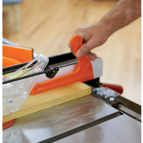 Hand using an orange three quarter inch V notch push stick for narrow stock on table saw, part of Must Have Power Tool Safety Set For Woodworking With Foam Grip Push Blocks Extra Long 16 Inch Push Block With Dual Handles Three Quarter Inch V Notch Push Stick For Narrow Stock And Eight And A Half Inch Saw Guide For Precise Table Saw Control