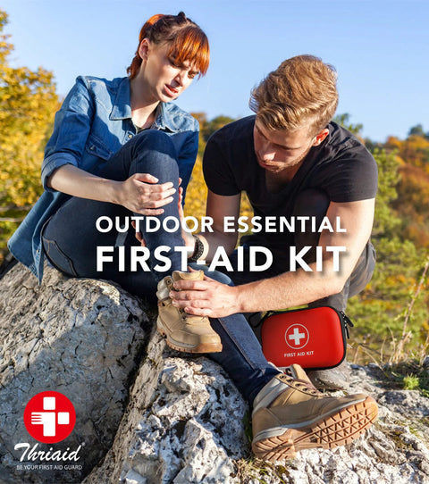 ThriAid mini first aid kit in a red hard-shell case with white cross logo, outdoors with hikers.