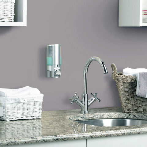 Satin Silver One Chamber Wall Mounted Soap And Gel Sanitizer Dispenser in bathroom above countertop with sink and baskets.