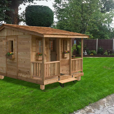 Wooden garden shed with porch and windows on a lawn under a cloudy sky.