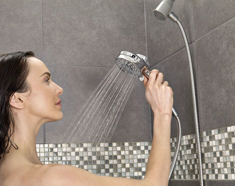 Person using a handheld showerhead in a tiled bathroom shower setup.