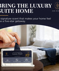 Hand holding Luxury Hotel Scent Whole Home Air Freshener System package in bedroom setting with spa-like decor.