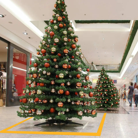 Decorated Christmas trees in a shopping mall with yellow floor marking tape forming a safety boundary.